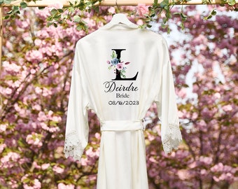 May include: White satin robe with lace trim, featuring a floral monogram with the letter "L" and the name "Deirdre Bride 08/16/2023".