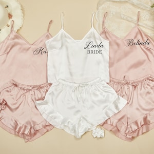 May include: Three sets of matching pink and white satin pajamas with lace trim. The white top has the text "Linda Bride" on it. The pink tops have the text "Ka" and "Belinda" on them.
