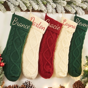 May include: Five knitted Christmas stockings with personalized names:  "Brance", "Daxton", "Gracie", "Layna", and "Steven". The stockings are green, white, red, white, and green.