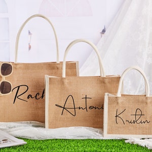 May include: Three brown burlap tote bags with white handles. The bags are personalised with the names "Rach", "Antoni", and "Kristin" in black script.