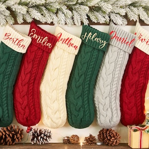 May include: Six personalized knitted Christmas stockings with names embroidered in red on the cuff. The stockings are in green, red, white, gray, and cream.