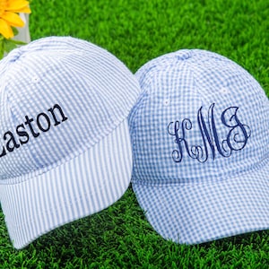 Könnte beinhalten: Zwei blau-weiß gestreifte Baseballkappen. Eine Kappe hat den Namen Easton bestickt. Die andere Kappe hat ein Monogramm bestickt.