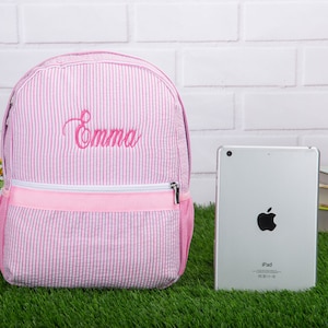 May include: Pink and white striped backpack with a pink zipper and the name "Emma" embroidered in pink on the front.