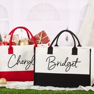 K&ouml;nnte beinhalten: Zwei personalisierte Tragetaschen mit roten und schwarzen Akzenten. Die Tasche links tr&auml;gt den Namen "Cheryl" in schwarzer Schrift auf wei&szlig;em Hintergrund mit rotem Boden. Die Tasche rechts tr&auml;gt den Namen "Bridget" in schwarzer Schrift auf wei&szlig;em Hintergrund mit schwarzem Boden.