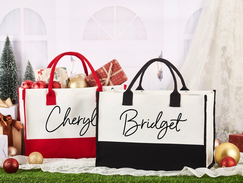 K&ouml;nnte beinhalten: Zwei personalisierte Tragetaschen mit roten und schwarzen Akzenten. Die Tasche links tr&auml;gt den Namen "Cheryl" in schwarzer Schrift auf wei&szlig;em Hintergrund mit rotem Boden. Die Tasche rechts tr&auml;gt den Namen "Bridget" in schwarzer Schrift auf wei&szlig;em Hintergrund mit schwarzem Boden.