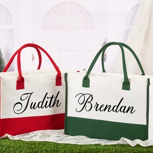 K&ouml;nnte beinhalten: Zwei personalisierte Canvas-Tragetaschen mit rotem und gr&uuml;nem Besatz. Die Tasche links tr&auml;gt den Namen "Judith" gestickt und die Tasche rechts tr&auml;gt den Namen "Brendan" gestickt.