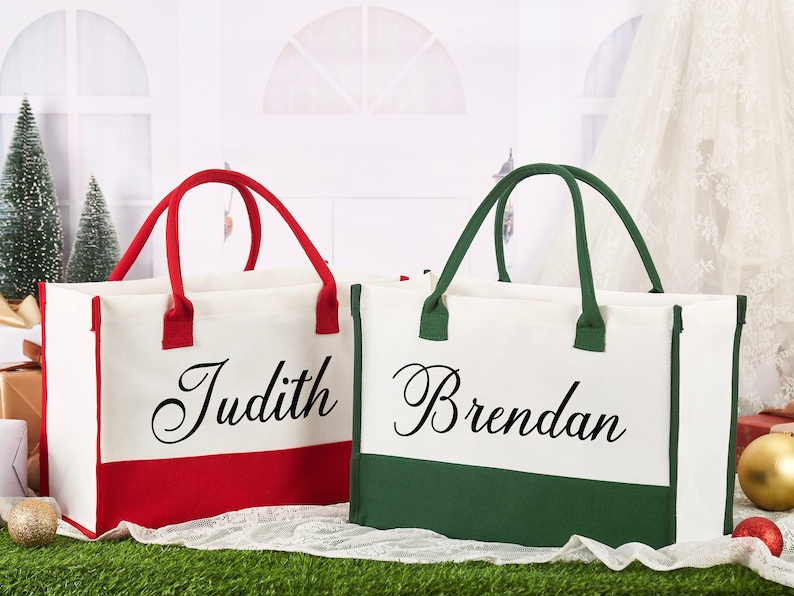 K&ouml;nnte beinhalten: Zwei personalisierte Canvas-Tragetaschen mit rotem und gr&uuml;nem Besatz. Die Tasche links tr&auml;gt den Namen "Judith" gestickt und die Tasche rechts tr&auml;gt den Namen "Brendan" gestickt.