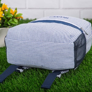 May include: A blue and white striped backpack with a mesh pocket on the side. The backpack has two adjustable straps.
