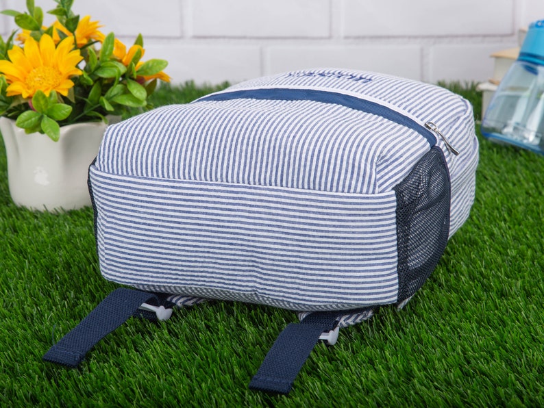 May include: A blue and white striped backpack with a mesh pocket on the side. The backpack has two adjustable straps.