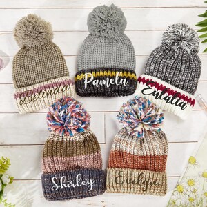 K&ouml;nnte beinhalten: F&uuml;nf gestrickte Winterm&uuml;tzen mit Bommeln und personalisierten Namen: Belinda, Pamela, Enaltia, Shirley und Evelyn.