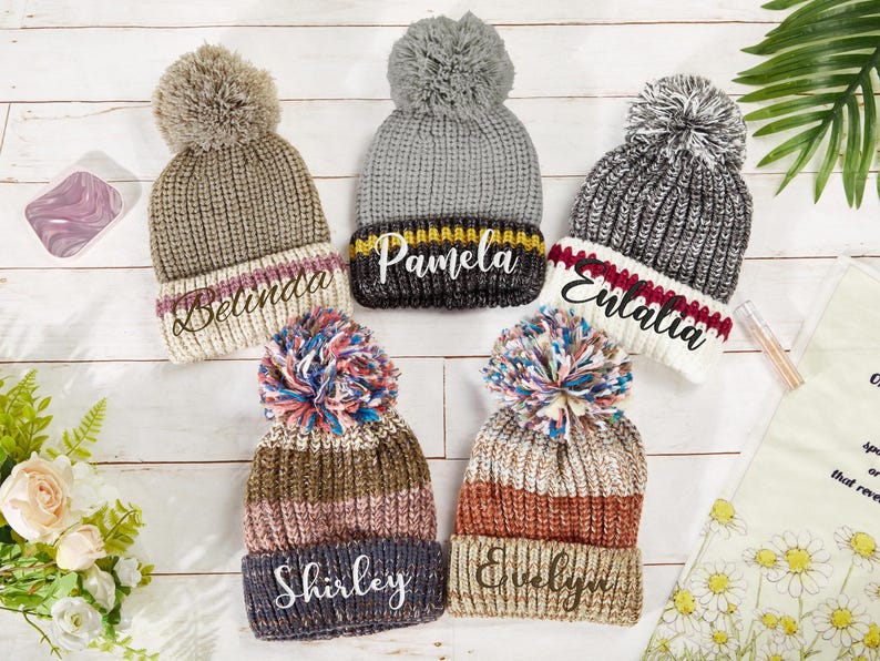 K&ouml;nnte beinhalten: F&uuml;nf gestrickte Winterm&uuml;tzen mit Bommeln und personalisierten Namen: Belinda, Pamela, Enaltia, Shirley und Evelyn.