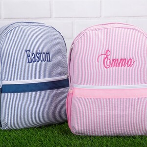 May include: Two personalized striped backpacks, one blue with the name Easton and one pink with the name Emma.