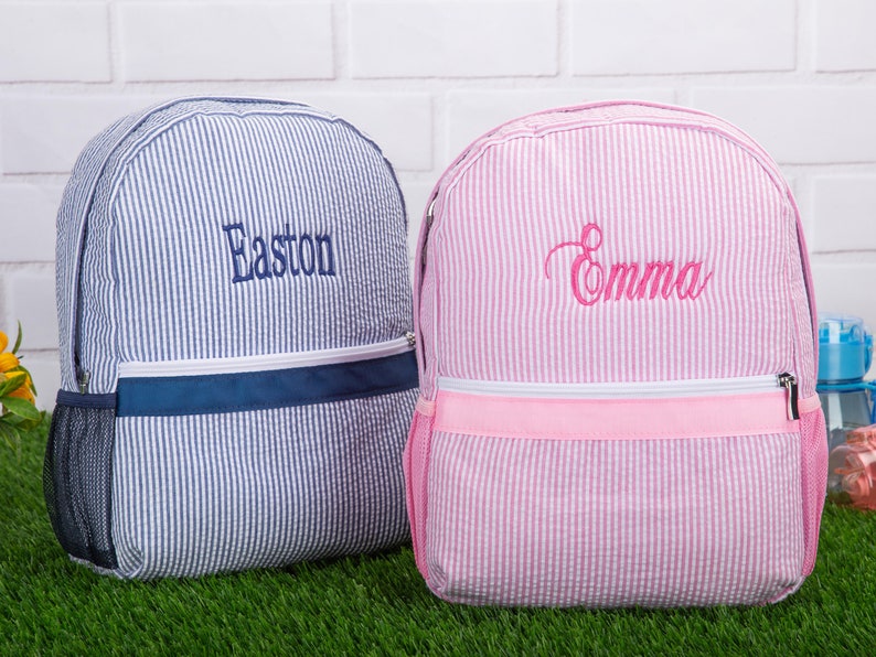 May include: Two personalized striped backpacks, one blue with the name Easton and one pink with the name Emma.
