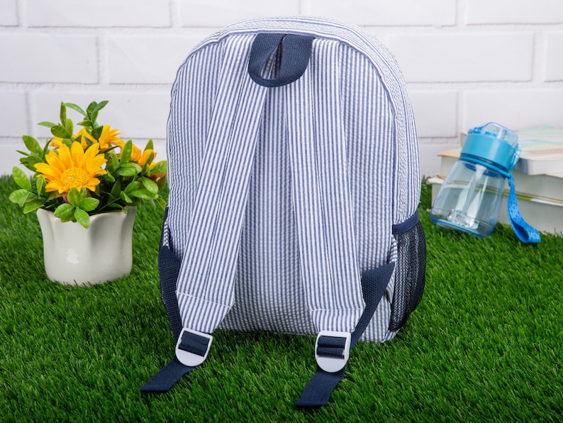 May include: A blue and white striped backpack with navy blue straps and a mesh pocket. The backpack has a top handle and adjustable straps.