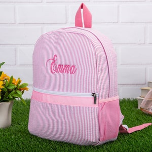 May include: Pink and white striped backpack with a pink zipper and a mesh pocket. The backpack is embroidered with the name "Emma".