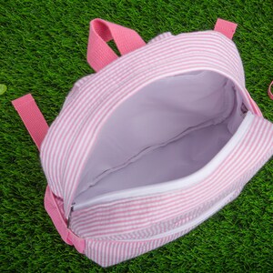 May include: A pink and white striped backpack with a zipper closure. The backpack is open and the inside is visible.