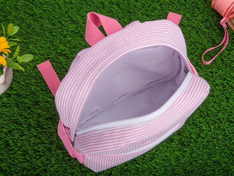May include: A pink and white striped backpack with a zipper closure. The backpack is open and the inside is visible.