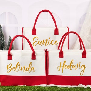 K&ouml;nnte beinhalten: Drei rote und wei&szlig;e Canvas-Tragetaschen mit goldener Beschriftung. Die Taschen sind mit den Namen Eunice, Belinda und Hedwig personalisiert.