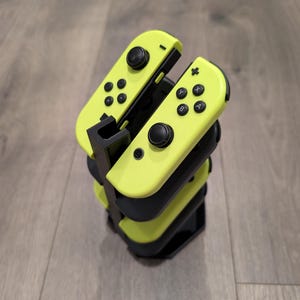 Peut inclure: Un support noir avec quatre manettes Nintendo Switch Joy-Con jaunes empilées les unes sur les autres.