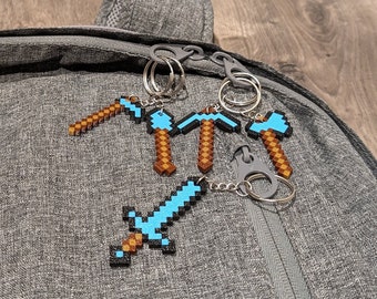 May include: A set of four Minecraft-themed keychains featuring a blue sword and three blue pickaxes with brown wooden handles. The keychains are attached to a gray backpack.
