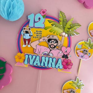 May include: A circular cake topper featuring a cartoon illustration of a person in a pink shirt and bucket hat, a palm tree, a pink heart, and the text "12", "DeBi TiRAR MaS FOTOS", and "IYANNA" in blue, accented with yellow, pink, and orange hibiscus flowers.