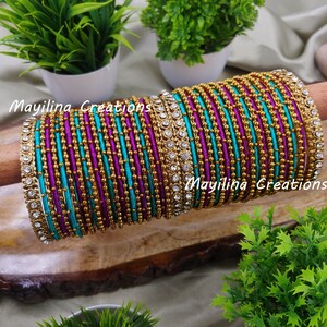 Puede incluir: Una pila de pulseras coloridas con detalles dorados y plateados. Las pulseras están hechas de hilo de seda y tienen un diseño de cuentas. Las pulseras están dispuestas en forma circular y se muestran sobre una superficie de madera. Mayilina Creations está escrito en la imagen.