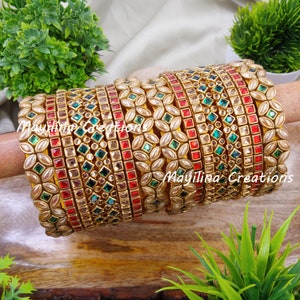 May include: A set of 12 gold bangles with red, green, and white stones. The bangles are stacked on top of each other and have a floral design.