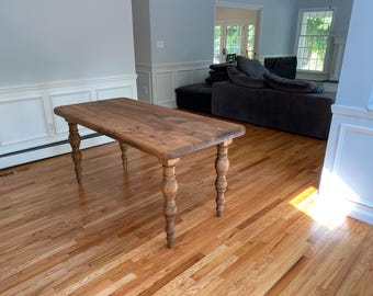 Op de afbeelding: Een rechthoekige houten tafel met een lichtbruine afwerking. De tafel heeft vier gedraaide poten en staat op een hardhouten vloer. De tafel is ongeveer 152 cm lang.