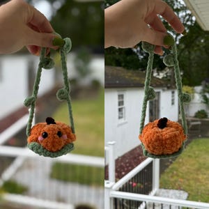 May include: A handmade crochet pumpkin bag in orange with a green base and stem. The pumpkin has a smiling face and is suspended by green vines with leaves. Perfect for Halloween or fall decor.