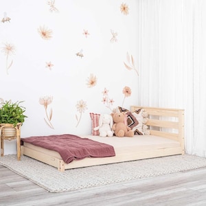 Peut inclure: Un lit plateforme en bois avec une finition brun clair. Le lit a une tête de lit à lattes et un profil bas. Le lit est recouvert d'une couverture rose et a deux animaux en peluche dessus. Le lit est dans une pièce avec des murs blancs et un rideau blanc.