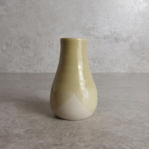 May include: A small, handcrafted ceramic vase with a rounded body and a narrow neck. The vase is primarily a soft yellow colour, with a white base. The vase is approximately 13 cm tall, suitable for displaying small flowers or decorative accents.