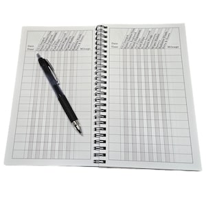 May include: An open spiral bound notebook with a black pen lying on the left page. The notebook is divided into columns with headings for date, time, and various car maintenance tasks, such as oil changes, tire replacements, and brake service. The right page has the same headings.