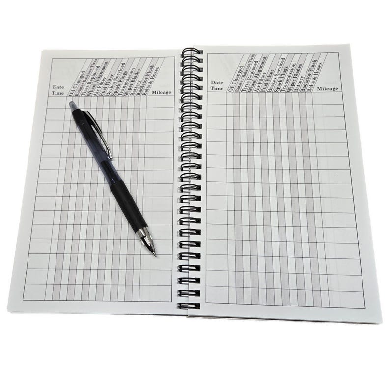 May include: An open spiral bound notebook with a black pen lying on the left page. The notebook is divided into columns with headings for date, time, and various car maintenance tasks, such as oil changes, tire replacements, and brake service. The right page has the same headings.