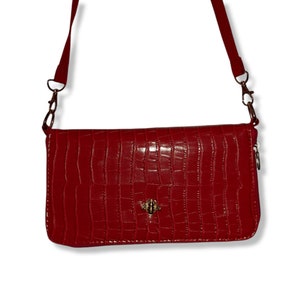 May include: A red crossbody bag with a crocodile-embossed texture and a gold bee charm.