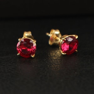May include: A pair of gold stud earrings with red gemstone accents.