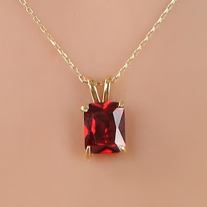 May include: A gold chain necklace with a red square-shaped gemstone pendant.