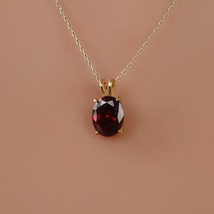 May include: A gold chain necklace with a round red gemstone pendant.