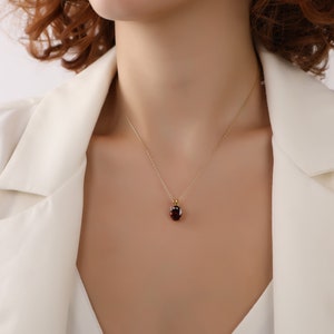 May include: A gold chain necklace with a red gemstone pendant. The pendant is a round, oval shape and is set in a gold setting.