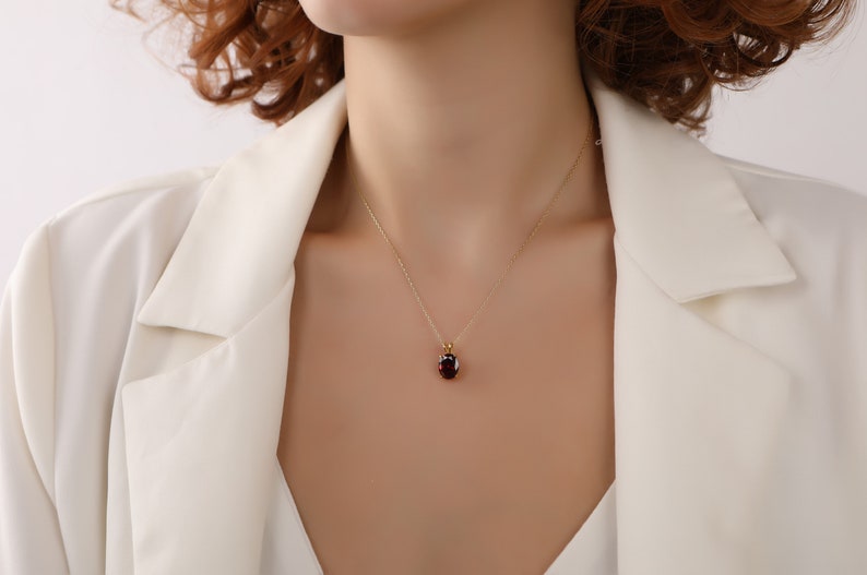 May include: A gold chain necklace with a red gemstone pendant. The pendant is a round, oval shape and is set in a gold setting.
