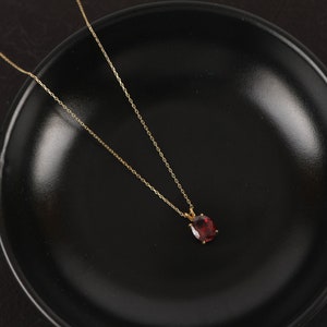 May include: A gold chain necklace with a red gemstone pendant. The necklace is on a black surface.