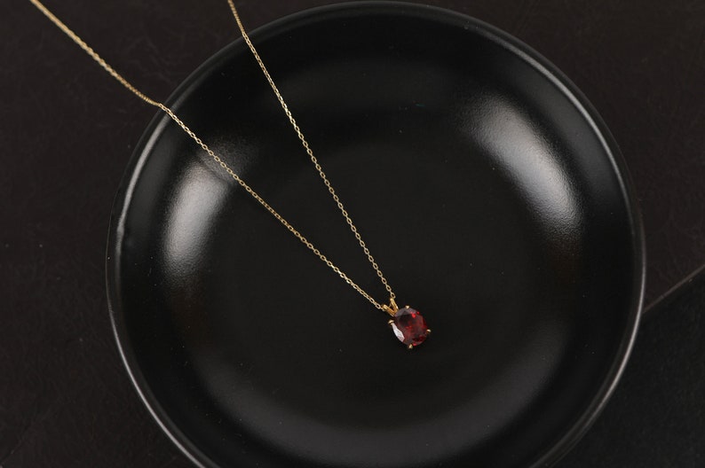 May include: A gold chain necklace with a red gemstone pendant. The necklace is on a black surface.