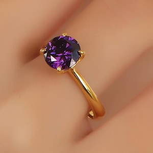 May include: A gold ring with a large, round, purple gemstone.