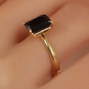 May include: A gold ring with a large, black, emerald-cut gemstone.