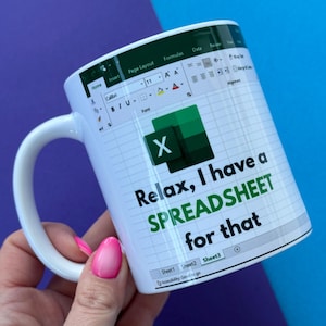 May include: White ceramic mug with an Excel spreadsheet design and the text "Relax, I have a SPREADSHEET for that." The mug has a white handle. The background is purple and blue.