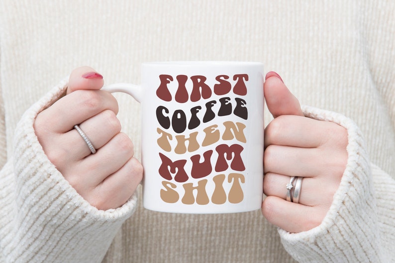 May include: White ceramic mug with the text "First Coffee Then Mum Shit" in brown, black, and red lettering. The letters are in a retro, wavy font.