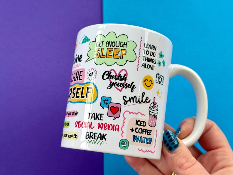 May include: White ceramic mug with a variety of colorful text and graphics, including "Get Enough Sleep," "Cherish Yourself," and "Smile." Other text includes "Take Social Media Break" and "Iced + Coffee Water."
