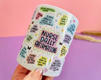 May include: White ceramic mug with colorful text and illustrations. The text reads "Nurse Daily Affirmations" and includes phrases like "I am an amazing nurse", "I have empathy for all of my patients", "I am a problem solver", "I trust myself", "I am grateful for all that I have", "I want to help and heal others", "It's okay to not feel okay", "I see the good in all situations", "I am doing my best everyday", "I am energized and ready to start my day", "I will not stress over things I can't control".