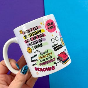 May include: White ceramic mug with colorful text and illustrations. The mug features phrases like "Don't let yesterday take up too much of today" and "Speak Kindly." Other text includes "read a book" and "Spend quality time with yourself reading."