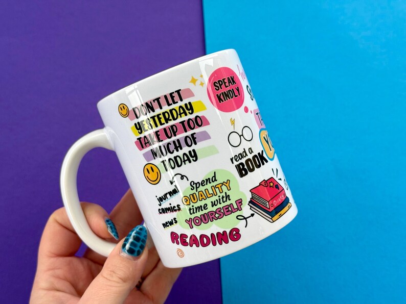 May include: White ceramic mug with colorful text and illustrations. The mug features phrases like "Don't let yesterday take up too much of today" and "Speak Kindly." Other text includes "read a book" and "Spend quality time with yourself reading."