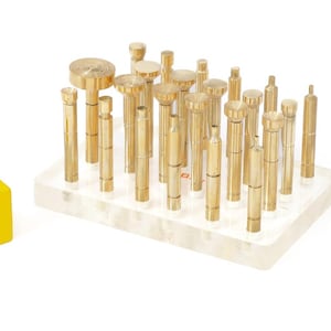 Puede incluir: Un conjunto de herramientas de latón, que incluye un bloque amarillo con el texto "WoHi", un conjunto de cilindros de latón de varios tamaños sobre un soporte transparente y una sola herramienta de latón con cabeza circular. Herramientas para joyería.